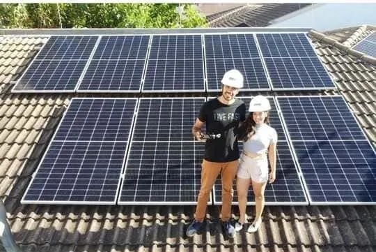 Bruno e Bruna, proprietários da SGT Energia Solar, de capacete sobre um telhado com placas solares instaladas